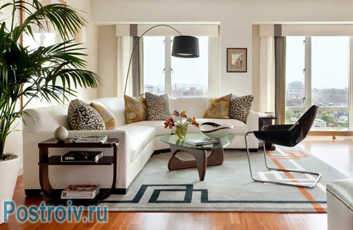Белый большой угловой диван и стеклянный столик в светлой гостиной